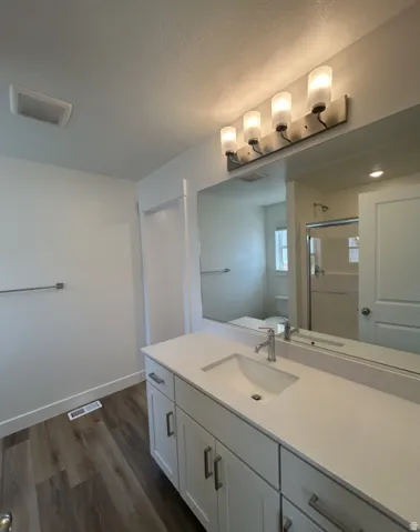 Spa-inspired primary bathroom featuring a generous quartz countertop with an undermount sink, white cabinetry with brushed nickel hardware, and a frameless glass-enclosed shower