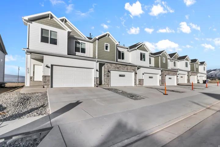 Contemporary townhome exterior featuring light siding, dark gabled roofing, a stone veneer facade, and an attached two-car garage