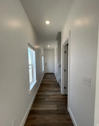Bright hallway showcasing rich wood-finish flooring, recessed ceiling lighting, and clean white walls with modern electrical outlets