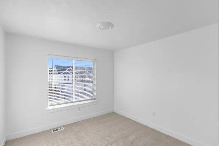 Bright corner bedroom with expansive windows featuring plantation shutters, neutral carpet flooring, and fresh white wall finishes