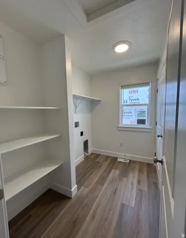 Spacious laundry area featuring built-in shelving, wood-finish flooring, and a window