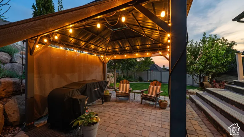 Expansive paver patio with a covered gazebo featuring string lighting, stone accent landscaping, and terraced stairs