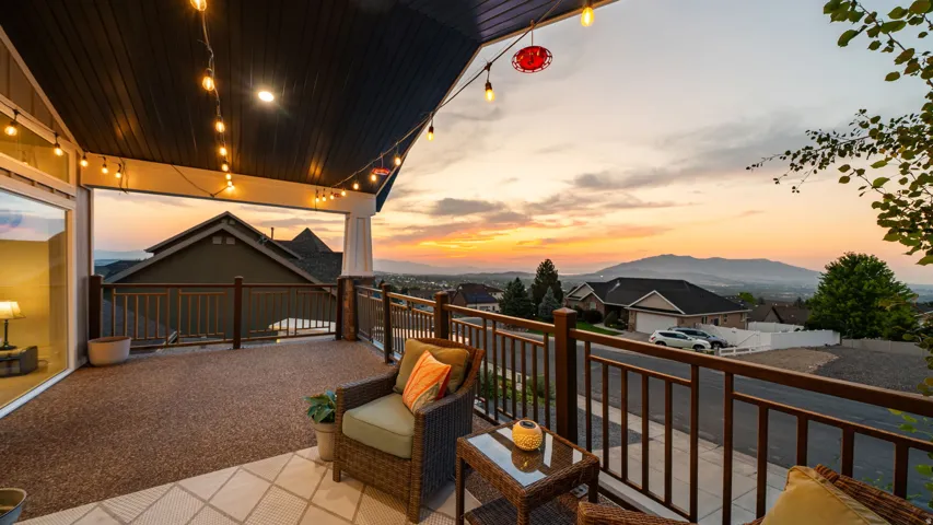 Covered outdoor deck with string lighting, finished flooring, and dark wood railings