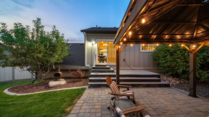 Paver patio with a built-in gazebo, wood-sided exterior, and a manicured lawn