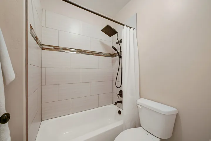 Bathtub with subway tile surround, mosaic accent band, and dark bronze shower fixtures