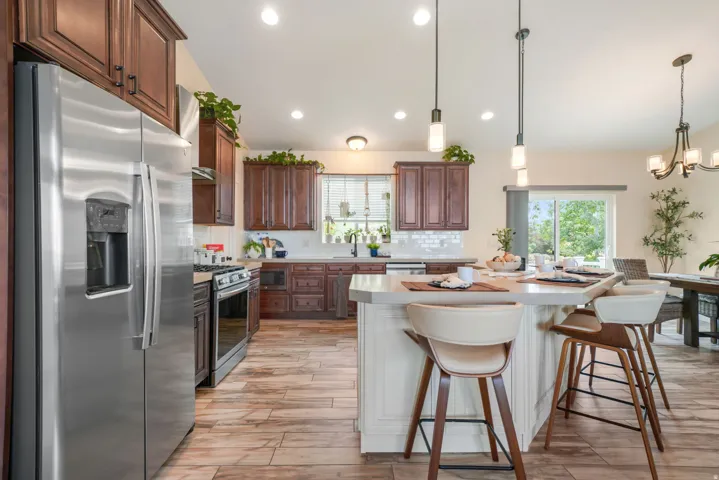 Stainless steel appliances, wood-finish flooring, dark wood cabinetry, a center island with pendant lighting, and a sliding glass door