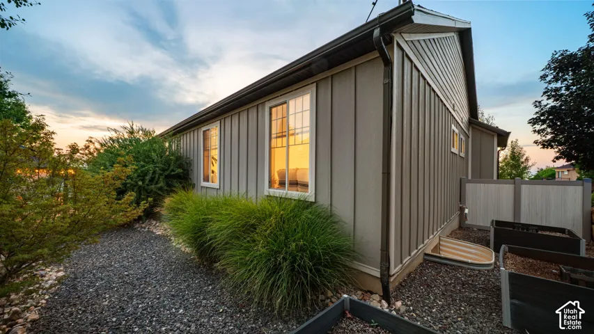 Board and batten siding with white-trimmed windows, dark gutters, and gravel landscaping