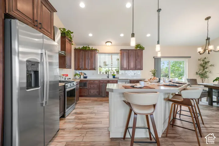 Stainless steel appliances, wood-finish flooring, dark wood cabinetry, a center island with pendant lighting, and a sliding glass door