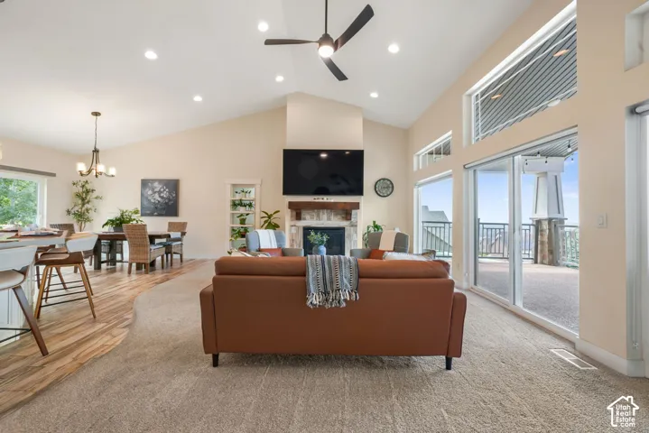 Vaulted ceilings with recessed lighting, large glass sliding doors, stone-faced fireplace with wood mantel, wood-finish flooring, and built-in shelving