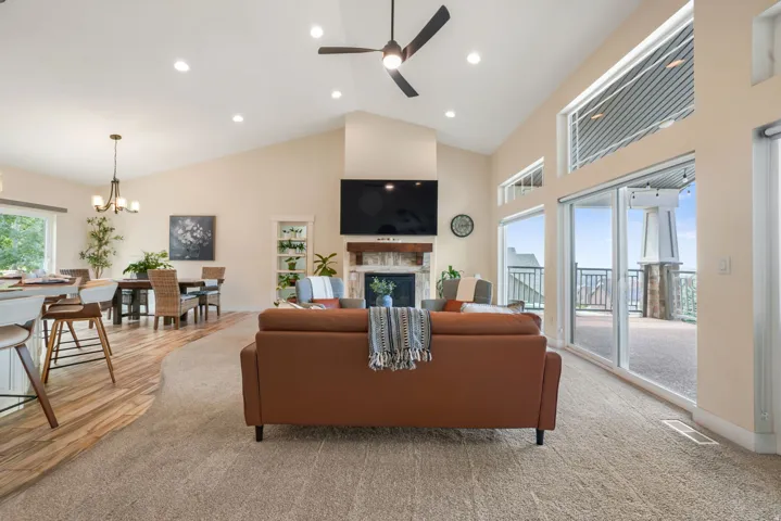 Vaulted ceilings with recessed lighting, large glass sliding doors, stone-faced fireplace with wood mantel, wood-finish flooring, and built-in shelving