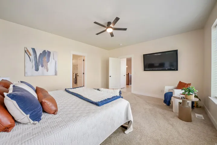 Carpeted room featuring a ceiling fan, a wall-mounted television, and an open doorway leading to a tiled interior space