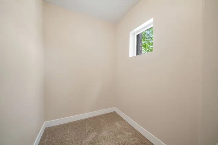 Compact room featuring neutral-toned walls, a single window, and carpet flooring