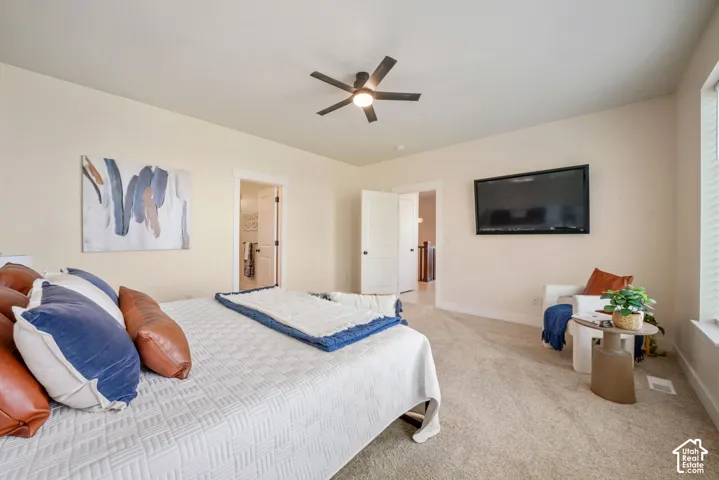 Carpeted room featuring a ceiling fan, a wall-mounted television, and an open doorway leading to a tiled interior space