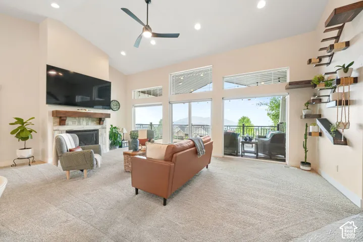 Vaulted ceilings, a stone-surround fireplace with wood mantel, recessed lighting, and expansive glass doors leading to an outdoor balcony