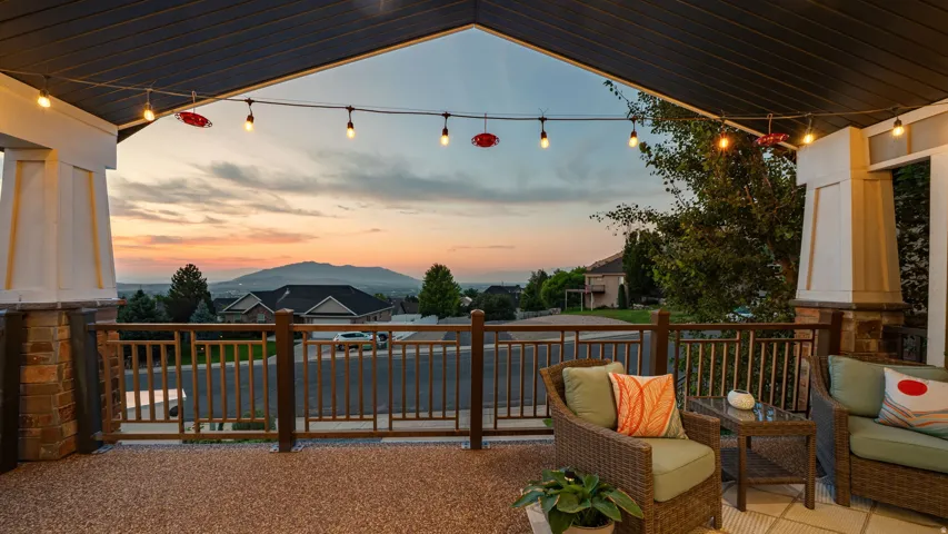 Covered outdoor patio featuring string lighting, stone column accents, and decorative railing