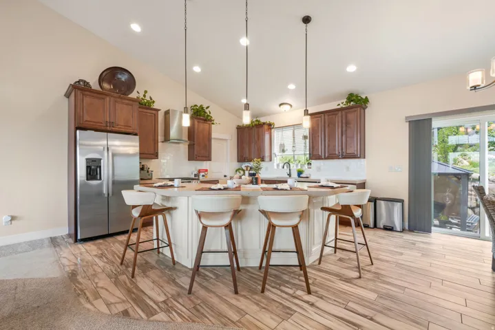 Kitchen with wood-finish flooring, recessed lighting, vaulted ceiling, built-in stainless steel appliances, and a central island with pendant lighting