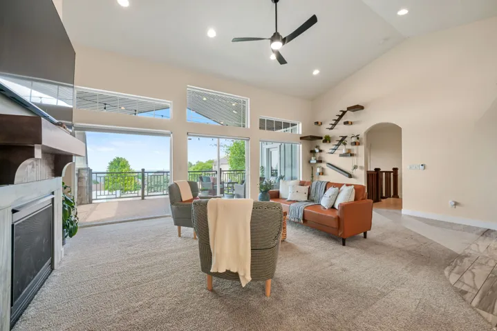 Soaring vaulted ceiling with recessed lighting, large glass sliding doors, built-in fireplace, contemporary ceiling fan, and arched doorway