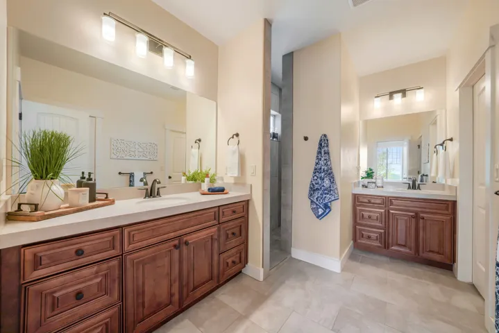 Dual wood-finish vanity cabinets with undermount sinks, stone countertops, and full-width mirrors
