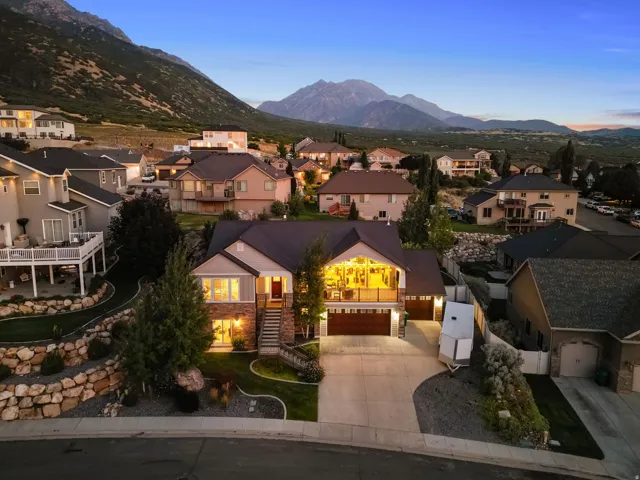 Contemporary residence featuring a prominent two-car garage, stone and siding exterior, front balcony, and mature landscaping