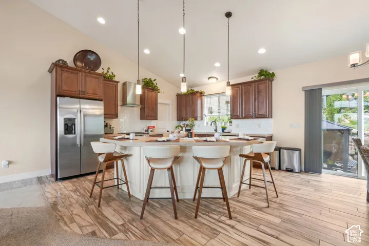 Kitchen with wood-finish flooring, recessed lighting, vaulted ceiling, built-in stainless steel appliances, and a central island with pendant lighting