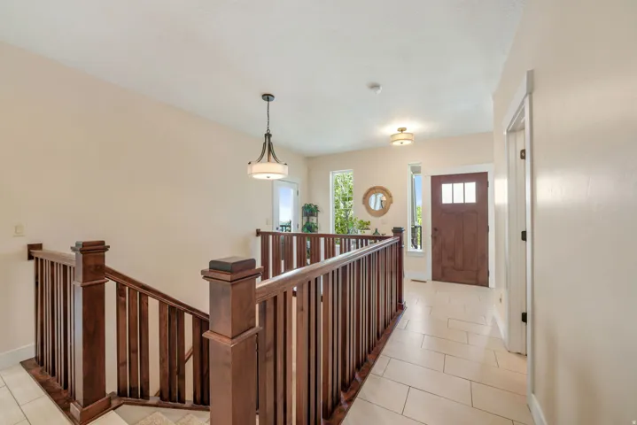 Rich wood-finish staircase and railing with square balusters, light tile flooring, and a solid wood-finish entry door with multiple glass panes