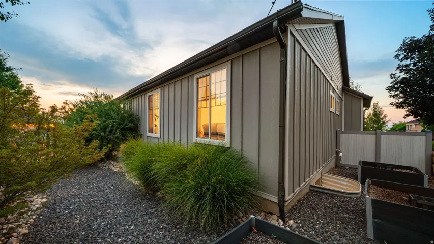 Board and batten siding with white-trimmed windows, dark gutters, and gravel landscaping