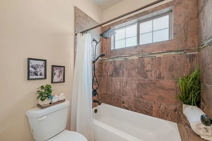 Built-in bathtub with a dark-tiled surround, mosaic tile accent band, and a window with privacy glass