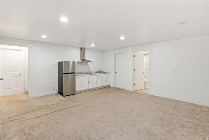 Open-plan living space with recessed lighting, integrated kitchen area featuring white cabinetry, stainless steel refrigerator, and range hood