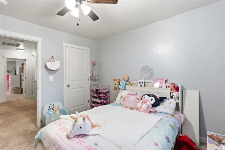 Bright secondary bedroom featuring neutral wall finishes, carpeted flooring, ceiling fan with integrated lighting, and ample natural light from windows