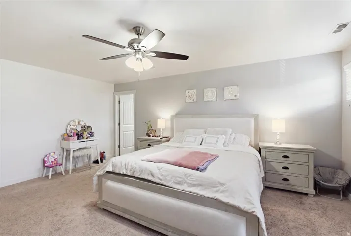 Spacious bedroom featuring neutral wall tones, carpeted flooring, and a ceiling fan with integrated lighting
