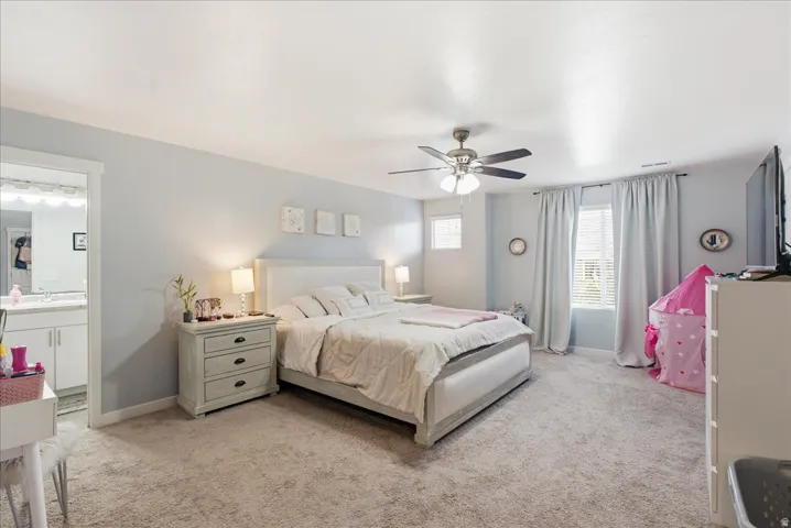 Neutral-toned carpeted flooring, a ceiling fan with integrated lighting, and light-colored window treatments