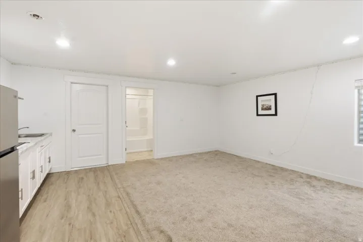 White cabinetry with a stainless steel sink, wood-finish flooring, and light-colored carpeting