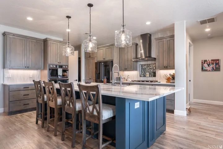 Spacious kitchen featuring a large central island, wood-finish flooring, undermount sink, stainless steel appliances, and custom cabinetry