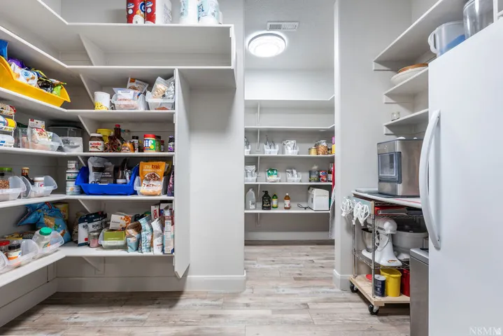 Extensive pantry featuring built-in shelving, wood-finish flooring, recessed lighting, and a white refrigerator