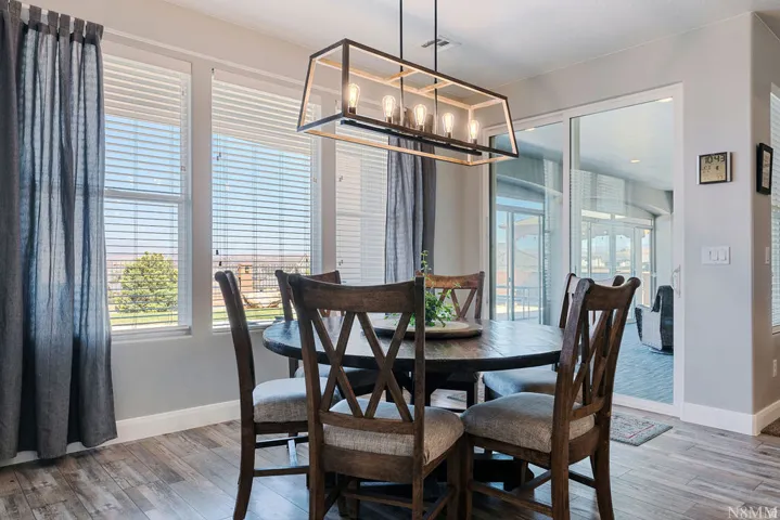 Wood-finish flooring with a multi-light linear chandelier, multiple windows with horizontal blinds, and a sliding glass door
