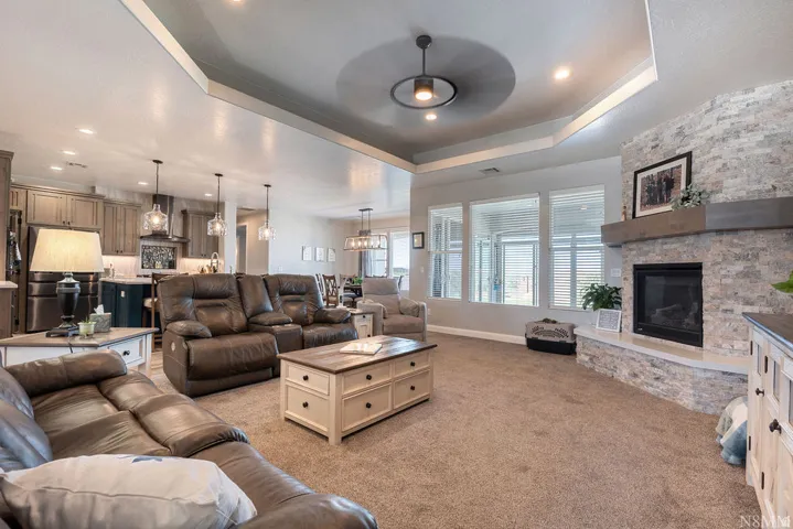Tray ceiling with recessed lighting, stone-clad fireplace with mantel, and large windows with blinds