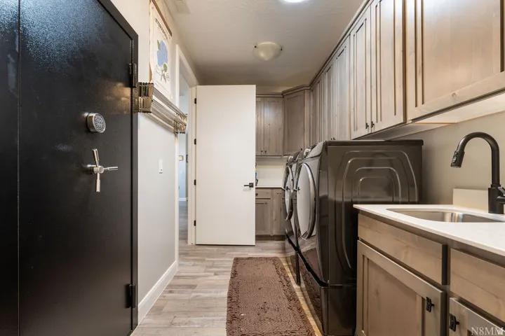 Dedicated laundry area featuring wood-finish cabinetry, a built-in sink with a gooseneck faucet, and wood-finish flooring