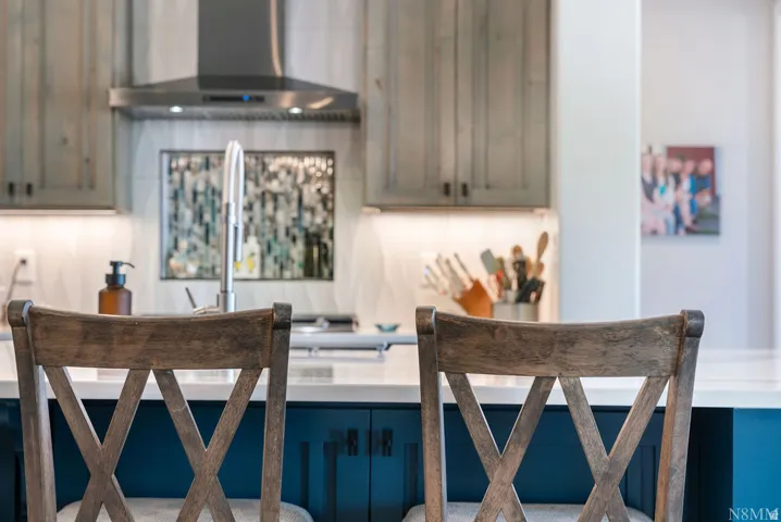 Kitchen with wood-finish upper cabinetry, stainless steel range hood, mosaic tile backsplash, and under-cabinet lighting