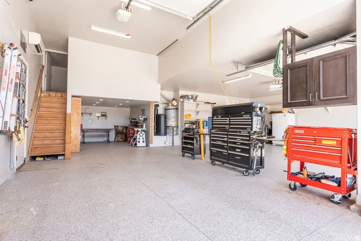 Expansive garage space with a speckled epoxy floor, natural wood staircase, built-in overhead cabinetry, and an integrated air conditioning unit