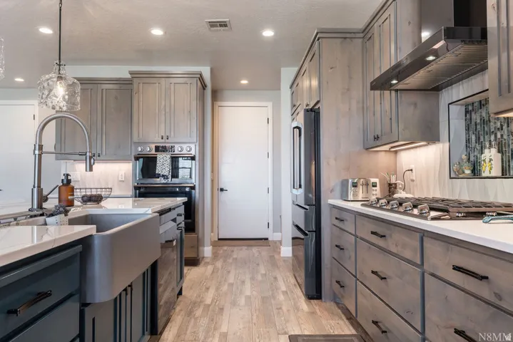 Kitchen featuring wood-finish flooring, stainless steel farmhouse sink, gray cabinetry, integrated oven, and a gas range with an overhead vent hood