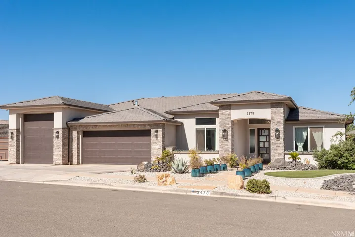 Contemporary stucco exterior with stone accents, a multi-pane front door, low-maintenance landscaping, and an attached two-car garage