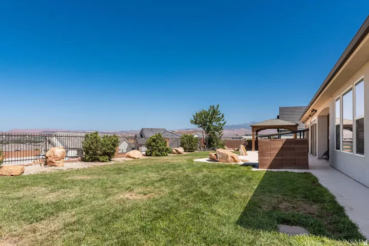 Expansive backyard featuring a manicured lawn, concrete patio, a gazebo structure, and a perimeter fence