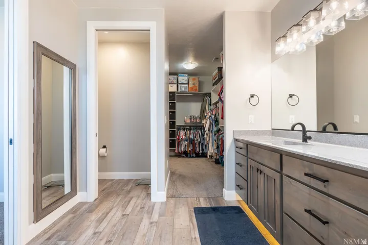 Dual sink vanity with stone countertop, wood-finish flooring, and a walk-in closet with built-in shelving
