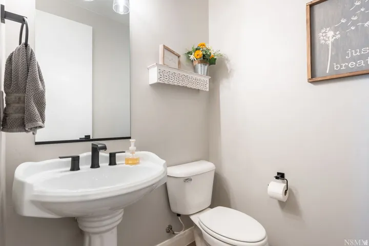 Pedestal sink with a matte black faucet, wall-mounted mirror, and white toilet