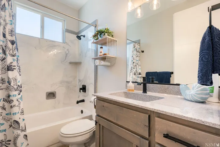 Bathroom featuring a white tub, an integrated vanity sink with a light-toned countertop, a large wall-mounted mirror, and a three-light fixture