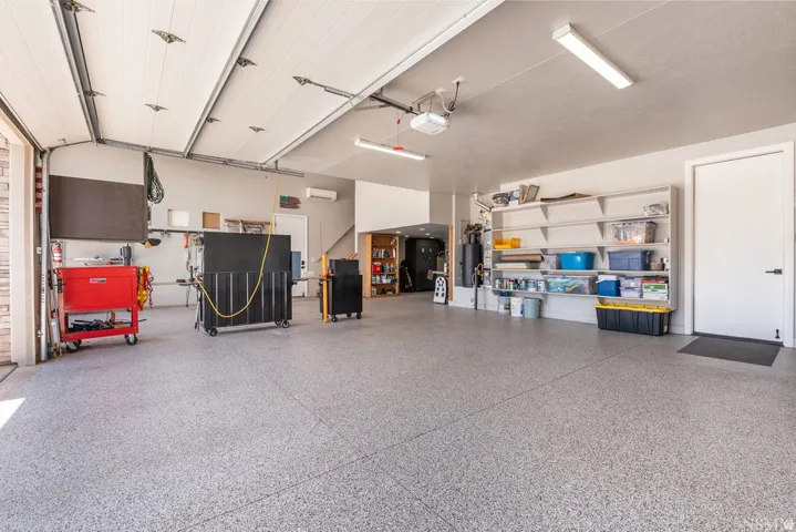 Spacious garage featuring a durable epoxy floor, integrated overhead lighting, and extensive wall-mounted shelving