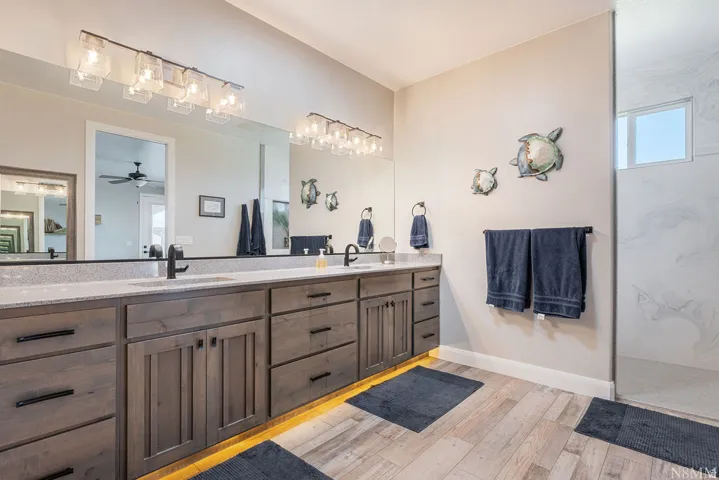 Wood-finish flooring, dual vanity with solid surface countertop, integrated sinks, matte black fixtures, and recessed lighting