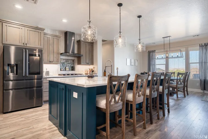 Gourmet kitchen with a center island featuring pendant lighting, stainless steel appliances, wood-finish flooring, and ample natural light