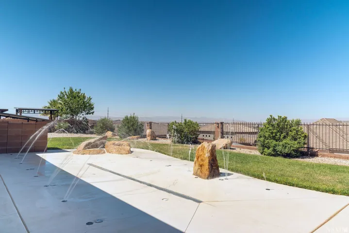 Concrete splash pad with water features, integrated natural rock elements, manicured lawn, and perimeter fencing