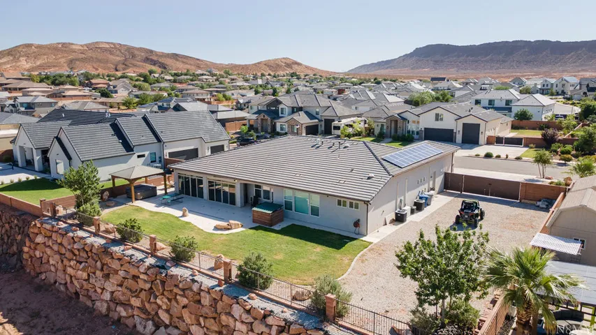 Contemporary residence featuring a low-slope roof with solar panels, a stone retaining wall, and an expansive paved outdoor area